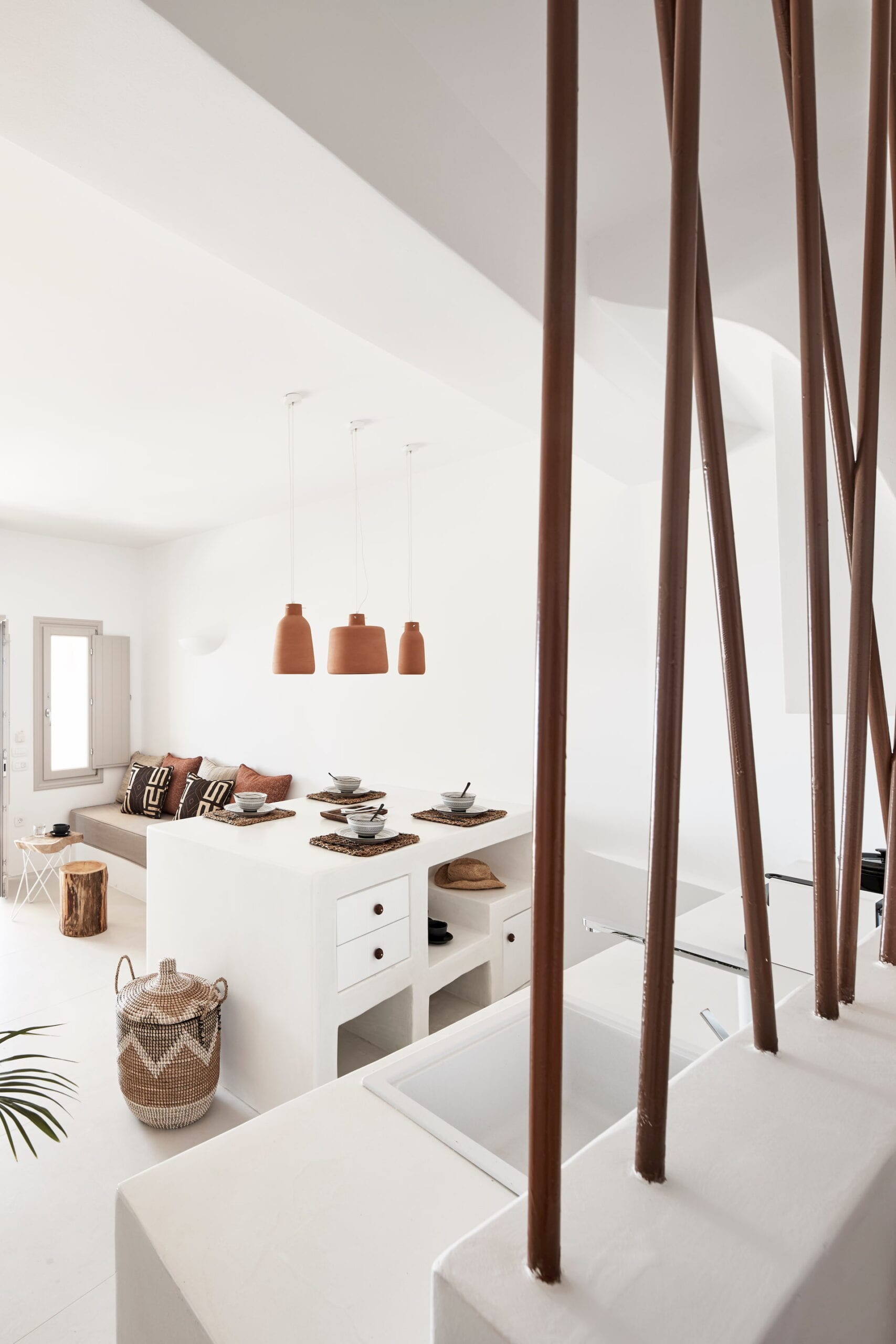 Whitewashed Cycladic living and dining space with terracotta pendant lamps and a sculptural floating staircase